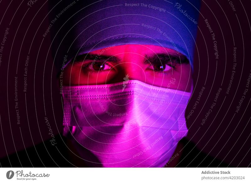Male doctor in mask in dark room with blue and red neon light surgeon man medical medicine protect illuminate sterile hospital treat clinic serious frown focus