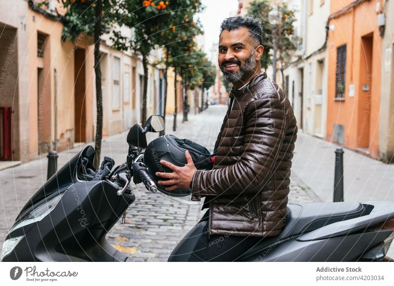 Smiling ethnic biker on modern motorcycle on city street motorcyclist masculine brutal smile virile macho man portrait content admire protective helmet town