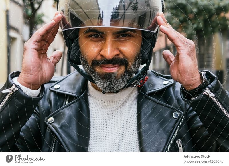 Smiling Hispanic biker putting on helmet on street put on cheerful brutal masculine virile man portrait friendly smile macho style modern motorcyclist content