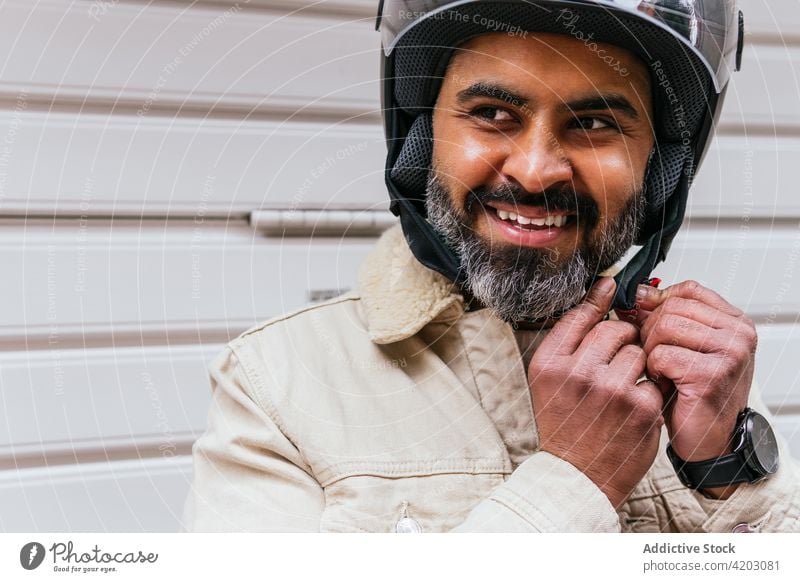 Smiling Hispanic biker putting on helmet on street put on cheerful brutal masculine virile man portrait friendly smile macho style modern motorcyclist content