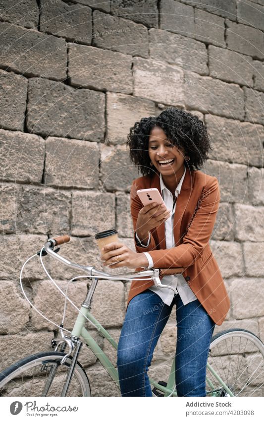 Cheerful black woman browsing smartphone near bicycle in city social media cheerful bike takeaway drink female ethnic african american parked device gadget