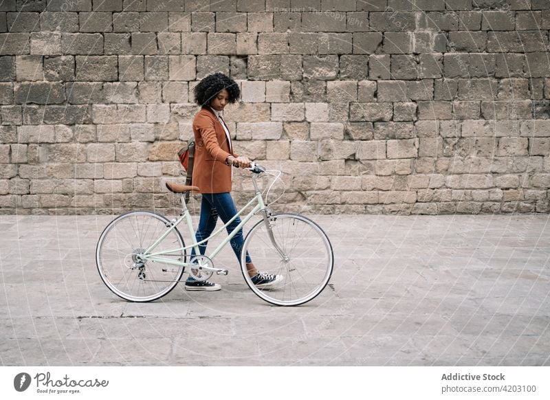 Ethnic woman walking with bicycle along street commute city smart casual bike trendy style female black african american ethnic urban contemporary vehicle town