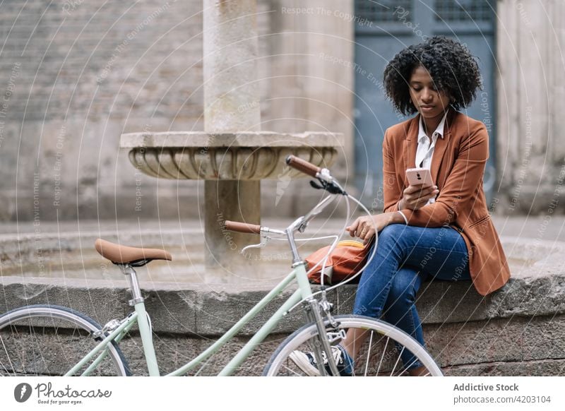Young black woman with bike using smartphone on street bicycle urban mobile browsing online young female african american student millennial gadget device