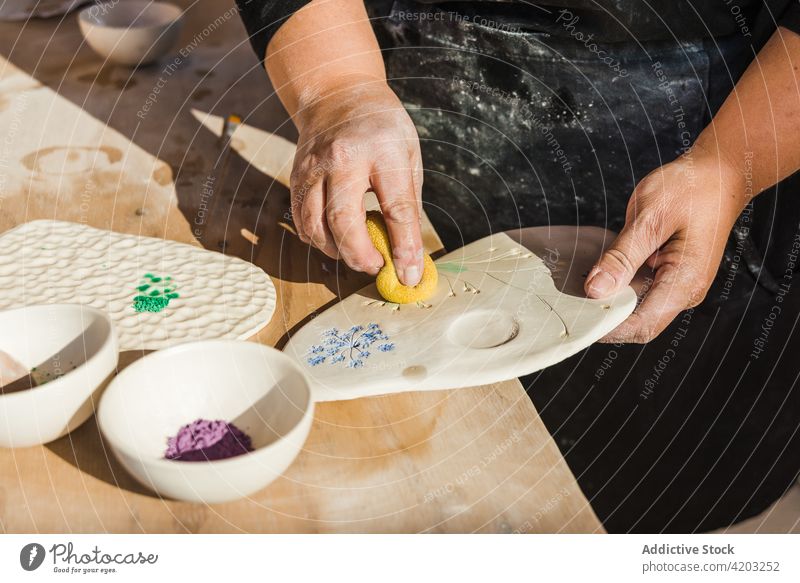 Unrecognizable woman filling in drawing on board with powder hobby sponge ceramic pigment palette art workshop craftswoman process female artisan dirty black