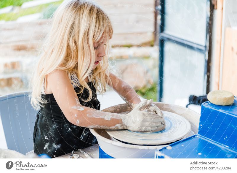 Little kid learning pottery at workshop wheel clay shape girl female child creative hobby little skill handmade dirty process vase table childhood talent apron
