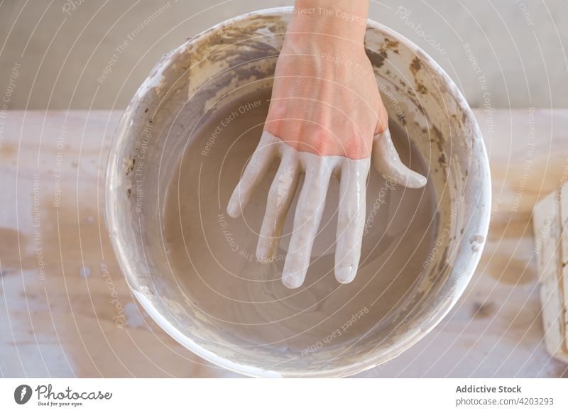 Faceless artisan pulling hand in clay from bucket in workshop woman hobby pottery craftswoman small business process female table daylight creative talent