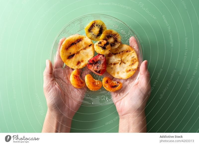Woman hands holding grilled fruit plate apple banana barbecue dessert eating food healthy kiwi mix orange pieces served strawberry summer sweet tangerine
