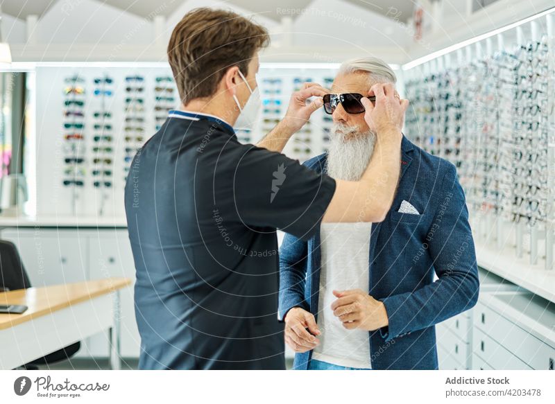 Optician helping aged man putting sunglasses in optical shop optician store senior put on customer service optometrist men male client elderly choose protect