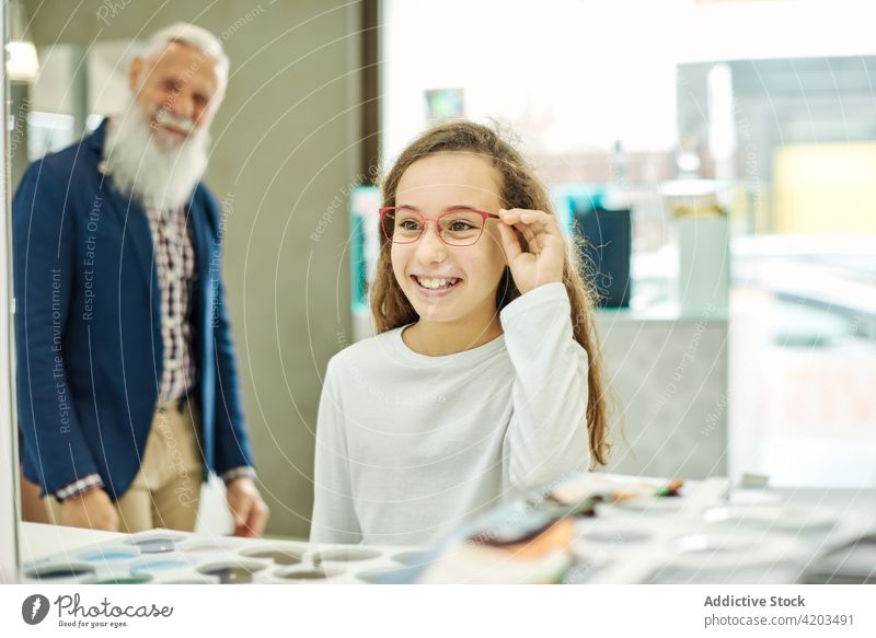 Girl choosing new glasses in optical store try on girl choose optician grandfather granddaughter together senior cheerful eyeglasses help mirror pick smile