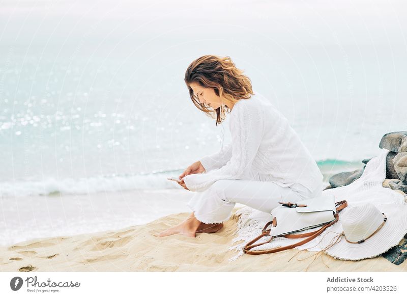 Carefree woman using mobile at seaside listen music tranquil harmony song calm serene beach female coast shore earphones device gadget ocean peaceful nature