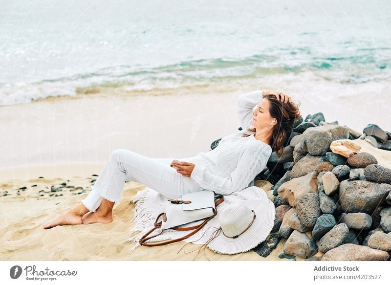 Carefree woman listening to music at seaside tranquil harmony song calm serene beach female lying coast shore earphones device gadget ocean peaceful nature