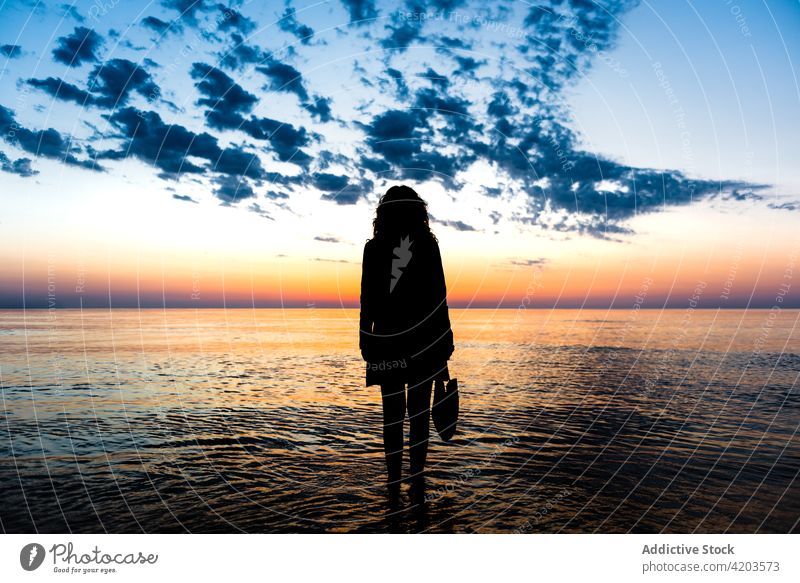 Anonymous woman standing against sea and sunset sky silhouette sundown twilight admire summer colorful female water tranquil scenery evening spectacular nature
