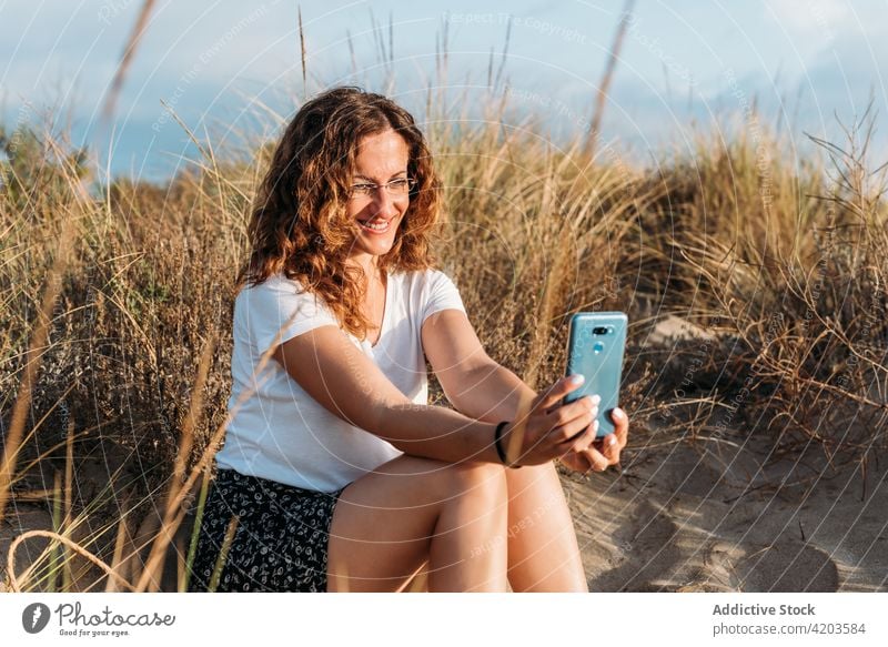 Woman taking selfie on beach at sunset woman smartphone browsing summer content using shore sand outfit mobile gadget evening vacation weekend tranquil message