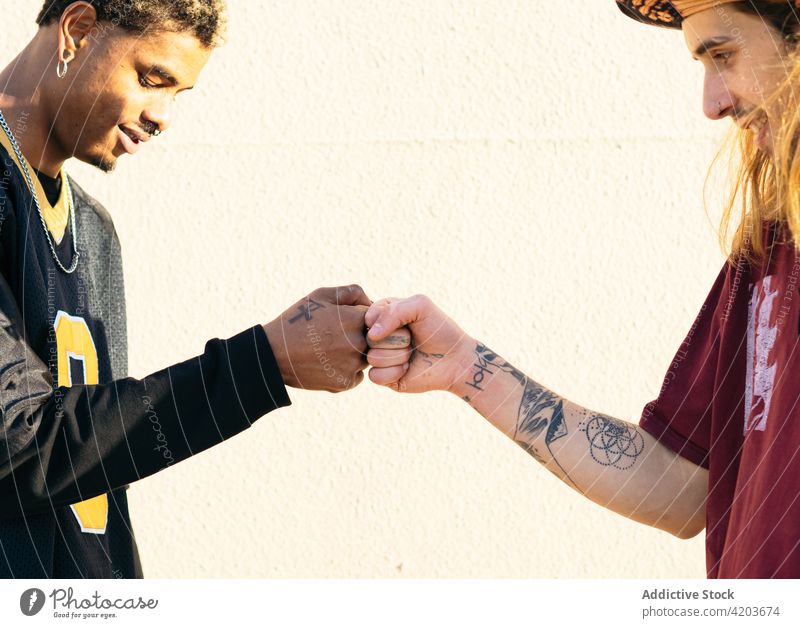 Crop multiethnic male friends bumping fists in sunlight fist bump greeting tattoo cool smile spend time weekend men portrait profile content enjoy multiracial