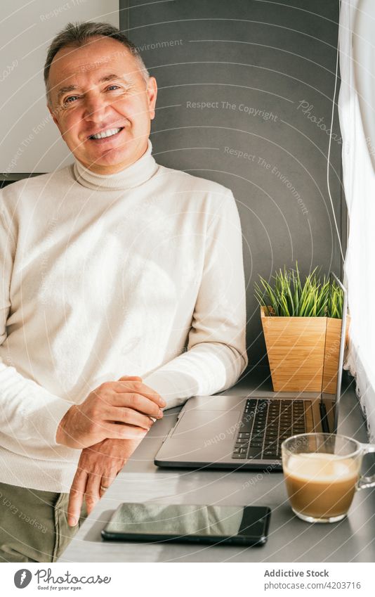 Cheerful mature man standing at counter with laptop in kitchen morning smile home breakfast coffee male lean cup netbook cheerful happy middle age device drink