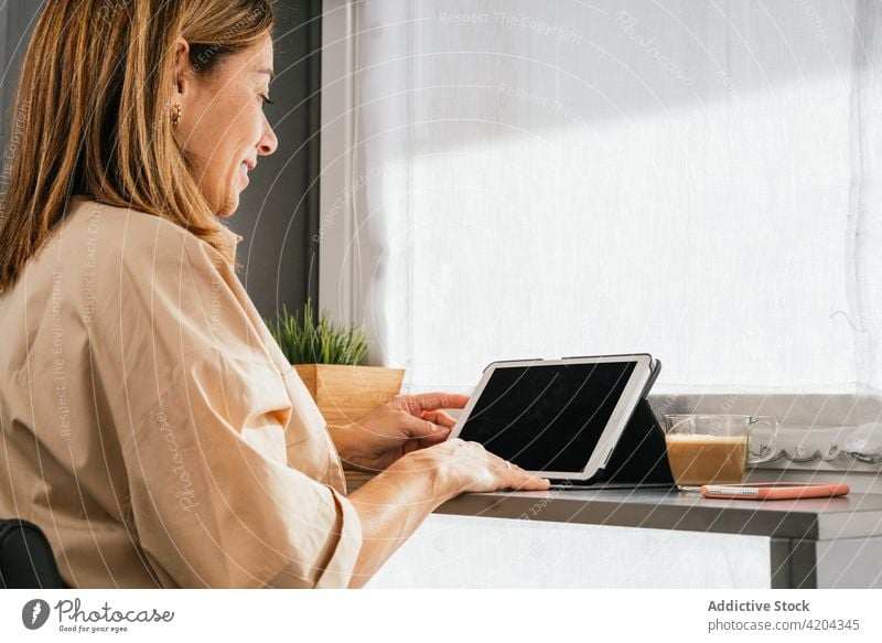 Smiling woman using tablet at counter in kitchen home mature browsing smile device female morning gadget middle age social media connection surfing internet