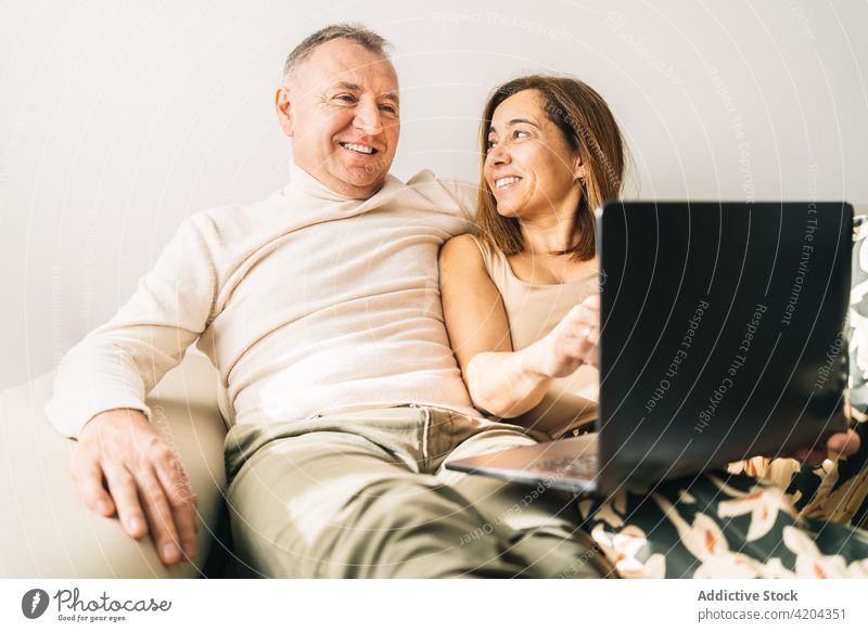 Content couple watching movie on laptop at home cuddle sofa weekend middle age living room cheerful together netbook gadget relax device couch relationship