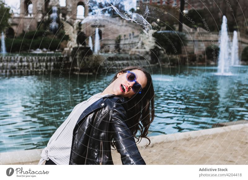 Carefree woman in city park near fountain carefree outstretch freedom stroll serene style outfit female trendy sunglasses garden appearance charming vogue