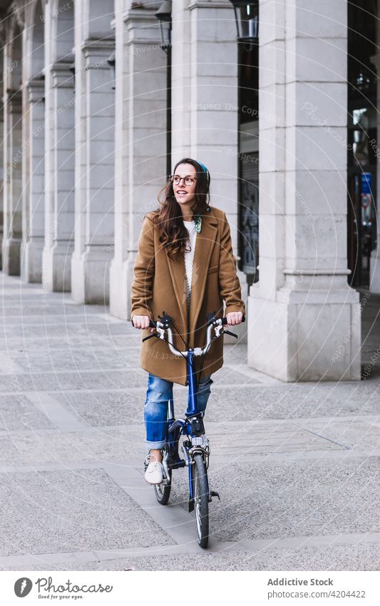 Smiling female biker on bicycle on city street smile colonnade architecture weekend spare time woman transport cheerful enjoy vehicle style lifestyle modern