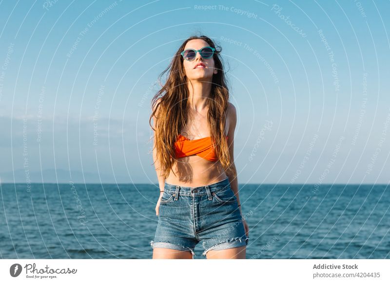Hipster woman in sunglasses standing on beach summer style hipster sea outfit trendy fashion young female eyewear eyeglasses accessory jeans lifestyle confident