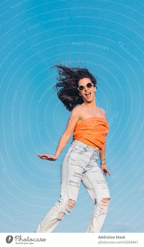 Hipster woman in trendy outfit jumping against blue sky summer style sunglasses fashion carefree hipster energy fly levitate happy casual young female eyewear