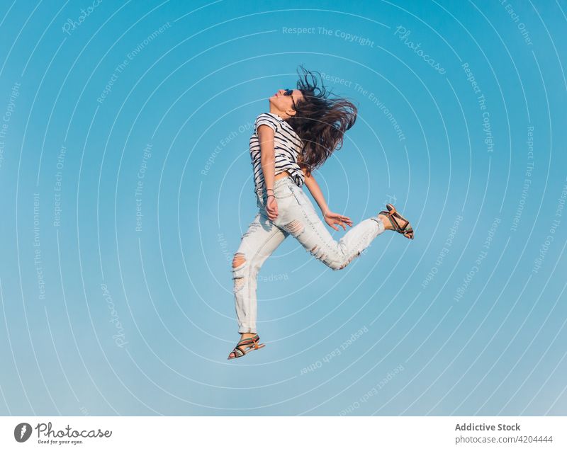 Hipster woman in trendy outfit jumping against blue sky summer style sunglasses fashion carefree hipster stripe energy fly levitate happy casual young female