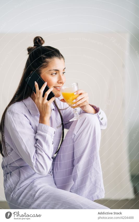 Charming woman with beverage on smartphone at home juice moment friendly charming using gadget device orange fresh glass refreshment speak healthy drink enjoy