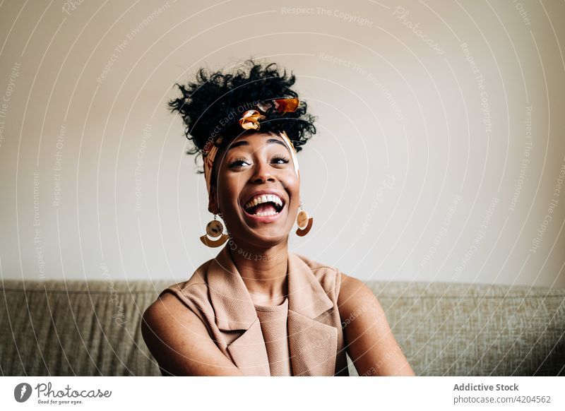 Serene black woman sitting on sofa and looking away home afro cheerful hairstyle toothy smile domestic happy serene calm female ethnic african american couch