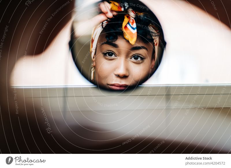 Charming black woman in headband looking in round mirror put on charming accessory headwear home content female ethnic african american reflection cheerful