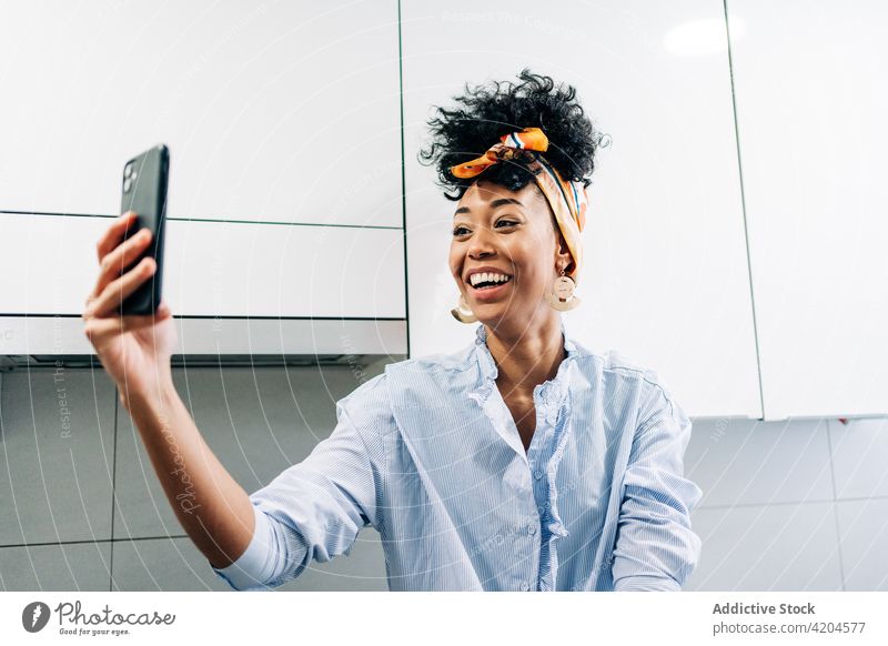 Content ethnic woman taking selfie in kitchen at home cheerful self portrait housewife positive smartphone headband female black african american using happy