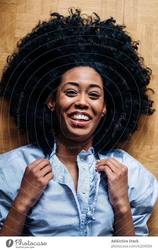 Content black woman lying on floor at home afro hairstyle tender serene slim curly hair cheerful appearance female ethnic african american toothy smile casual