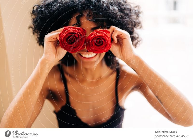 Delighted black woman with rose flowers cover eyes hide having fun red bud romantic cheerful female ethnic african american afro hairstyle home blossom floral