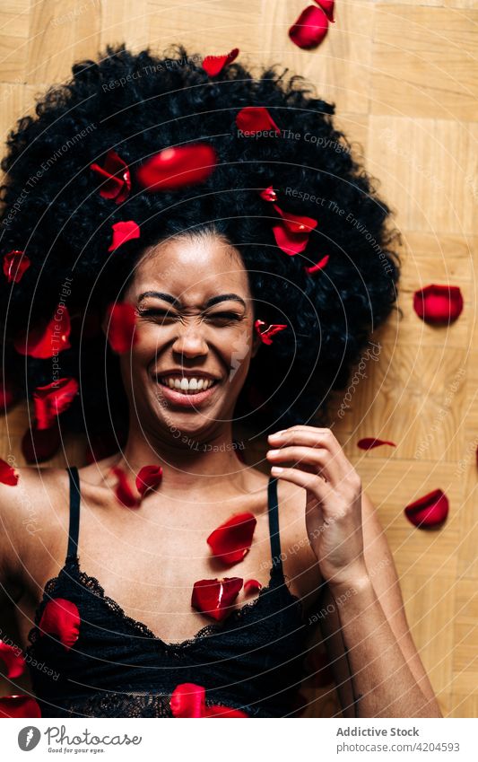 Happy black woman on floor covered rose petals heart gesture love romantic valentine tender female ethnic african american eyes closed valentine's day lying