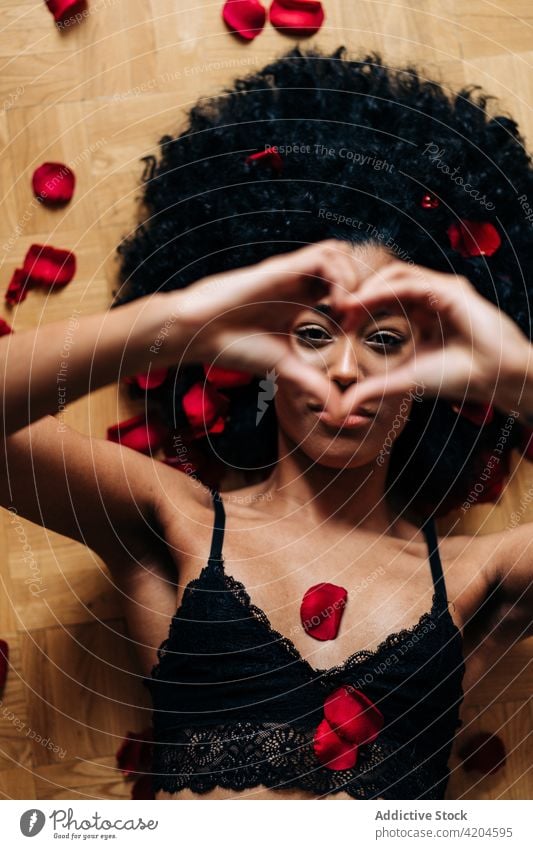 Black woman showing heart gesture on floor with rose petals love sign romantic valentine tender female ethnic black african american lying red afro hairstyle
