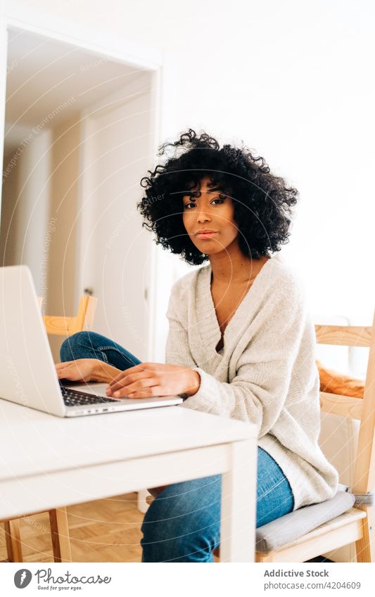 Content black woman sitting at table with laptop freelance cheerful home office entrepreneur project female ethnic african american device gadget remote work