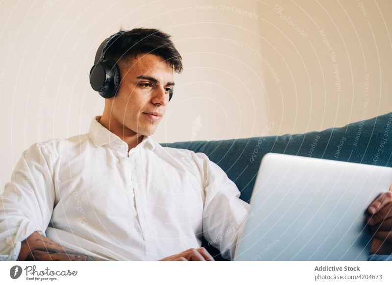 Focused man in headphones browsing laptop internet couch netbook online music remote surfing gadget listen sofa device home apartment living room computer
