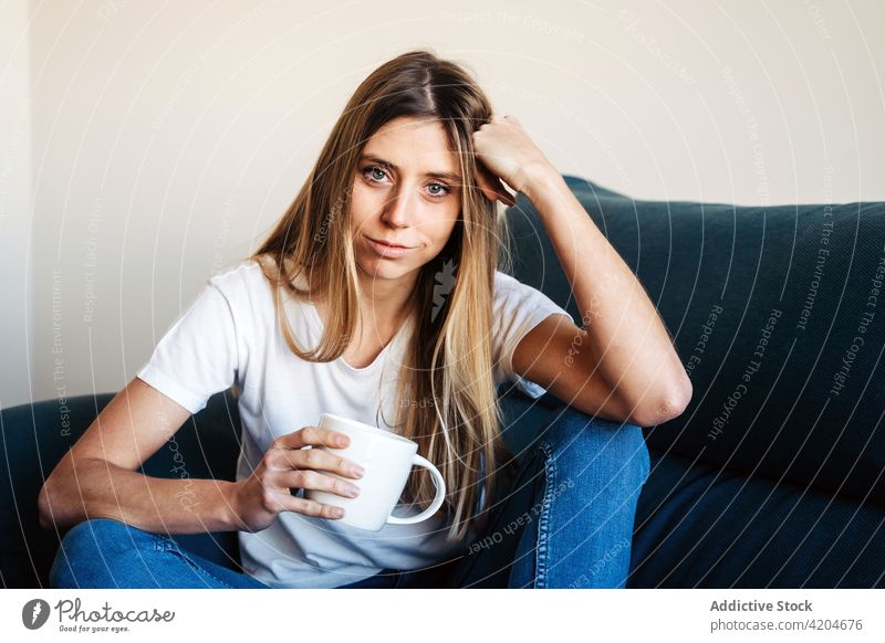 Calm woman with cup on sofa couch drink beverage coffee mug lean on hand leg bent lady female pensive lifestyle relax rest young calm leisure home break
