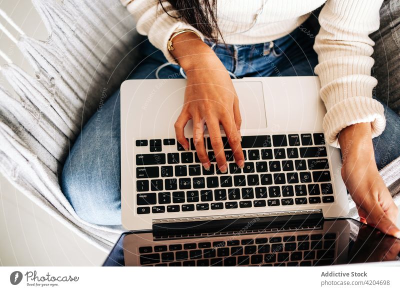 Anonymous young woman working on laptop while sitting in hammock freelance browsing gadget social media using comfort netbook female surfing online device