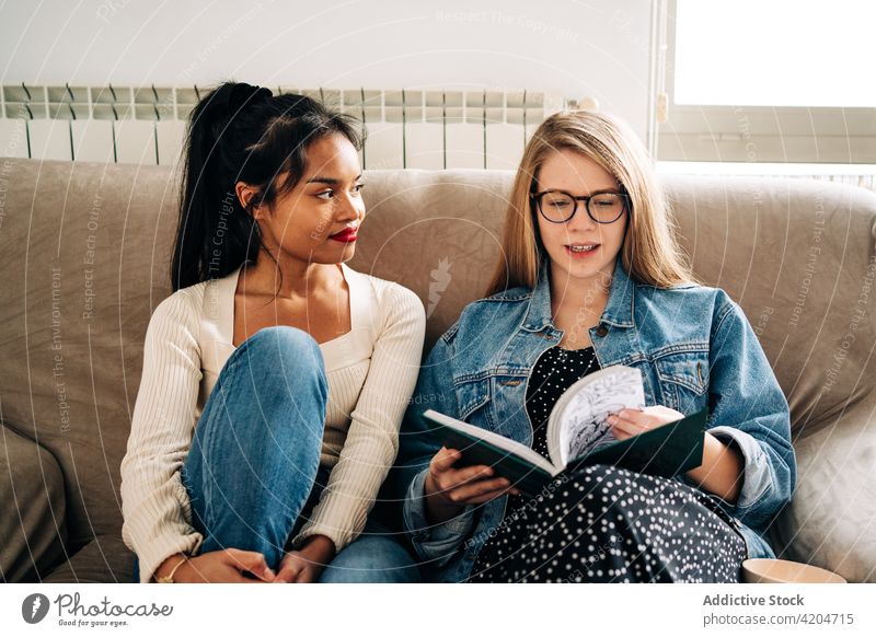 Pensive women on sofa reading book relax rest wistful spend time novel thoughtful ponder female multiracial multiethnic diverse friendship pastime young comfort