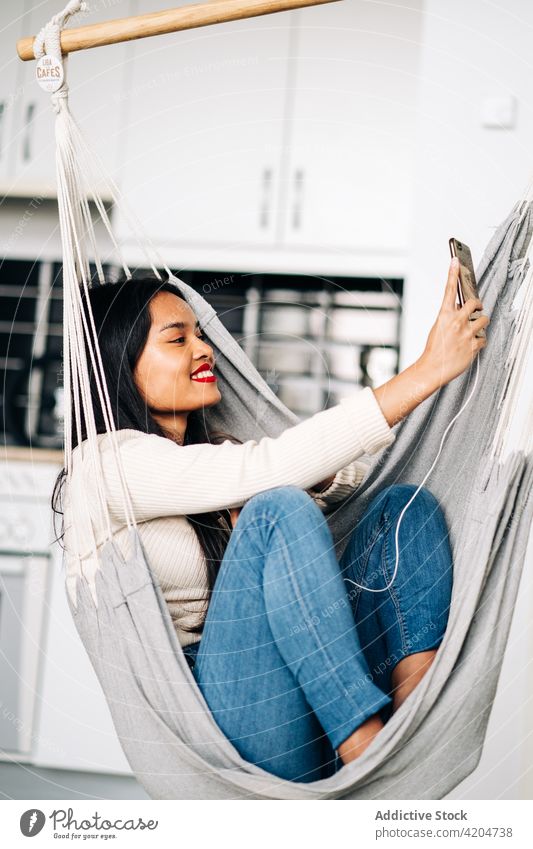 Cheerful woman in hammock having video call smartphone happy cheerful communicate online talk optimist female smile device gadget young connection joy enjoy
