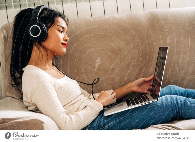 Dreamy woman with laptop and headphones sofa online internet using surfing watch break female browsing gadget connection netbook couch work chill contemporary