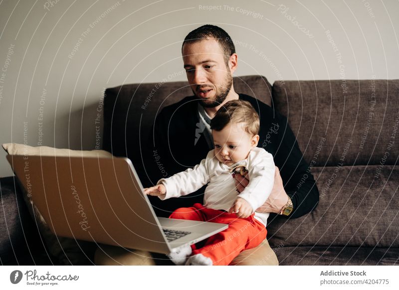 Young father with little son watching video on netbook man child cartoon laptop together love sofa relationship home online bonding young baby hug parent couch