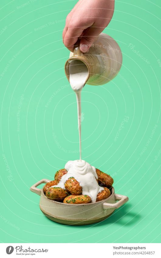 Pouring sour cream over roasted potatoes, minimalist on a green background. baby potato baked bowl ceramic close-up color copy space cuisine cut out delicious