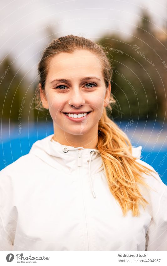 Cheerful sportswoman smiling and looking at camera athlete smile content sunny stadium sportswear professional training fit female healthy fitness happy