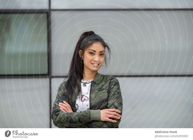 Confident Asian woman on city street urban style confident arms crossed outfit building wall female young ethnic asian trendy camouflage jacket modern exterior