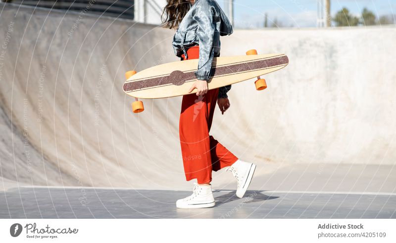 Excited woman with longboard jumping against leafless trees in town stylish athlete trendy walk style enjoy cool individuality gumshoe skateboarder wellness