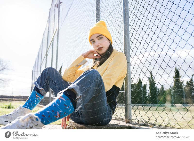 Stylish teen resting near fence in city teenage style cool trendy individuality casual lean on hand town portrait red lips yellow outfit sock grid metal sky