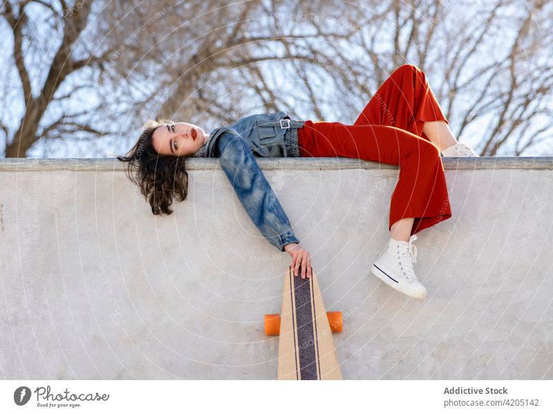 Skateboarder with longboard resting on skate ramp woman skateboarder sport tired exhausted sky skate park urban sportswoman stylish cloudy athlete trendy style