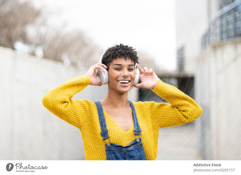 Happy black woman listening to music in headphones in city dreamy enjoy song wireless carefree female ethnic african american street pleasure tune smile audio