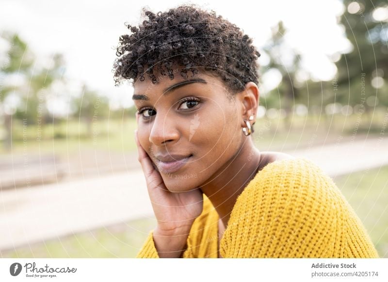 Charming black woman looking at camera in park charming afro appearance beauty hairstyle cool outfit garden female ethnic african american trendy smile glad